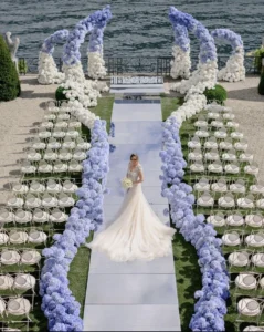 Luxury waterfront ceremony with a long blue aisle and floral arches