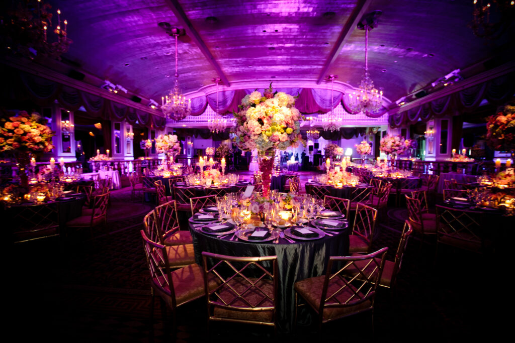 Dramatic wedding reception design with colorful lighting, floral centerpieces, and elegant table decor.