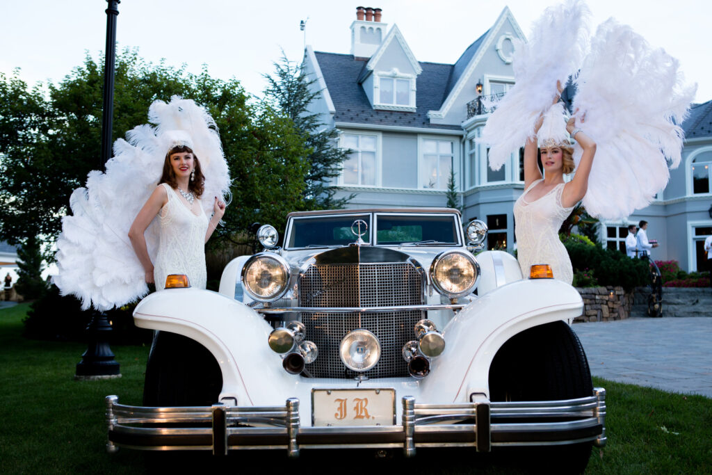 Costumed performers beside a vintage car at the entrance to an elegant corporate gala.