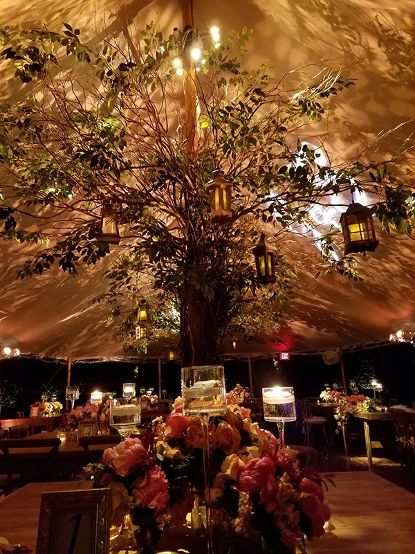 Tented wedding interior with ambient lighting, floral decor, and suspended lanterns.